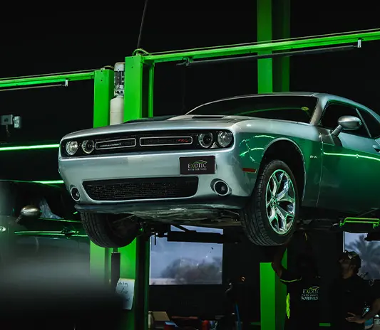 Silver Dodge car on a lift undergoing maintenance at a professional workshop.