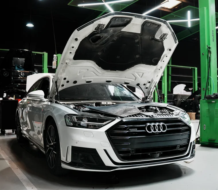 White Audi A8 with the bonnet raised for engine inspection inside the Exotic Auto Services workshop in Mussafah, Abu Dhabi.