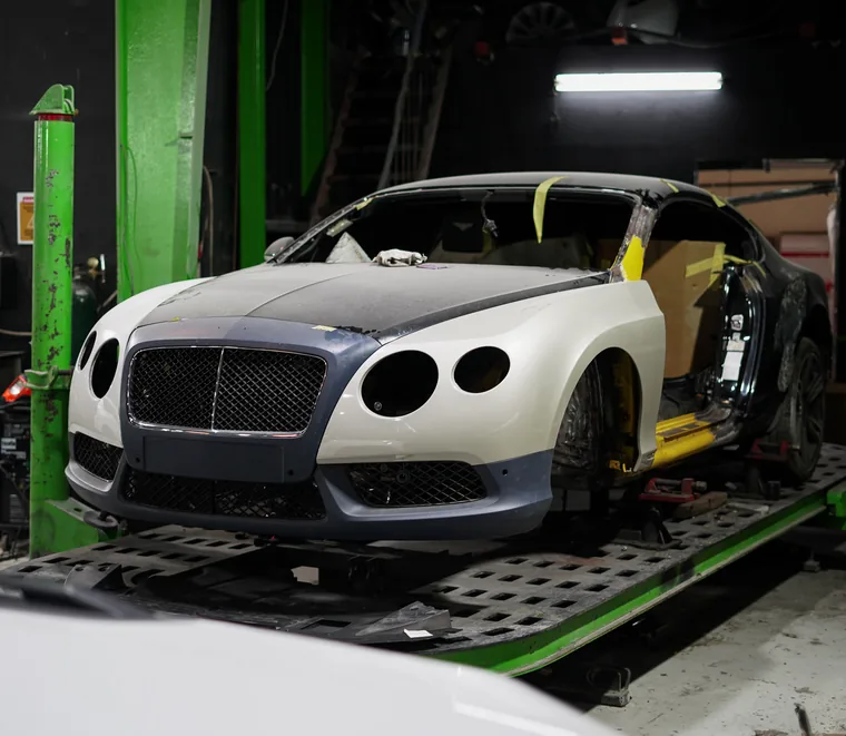 Bentley Continental GT stripped and masked for body and paint preparation on a bench in the Mussafah workshop.