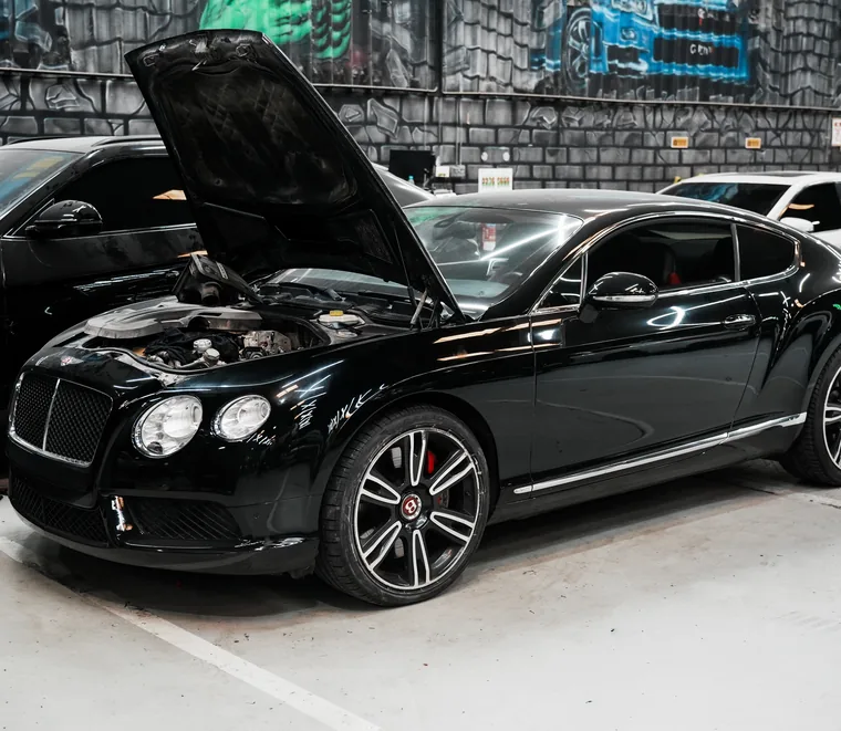 Black Bentley Continental GT with the bonnet raised for engine bay inspection at the Exotic Auto Services workshop in Mussafah, Abu Dhabi.