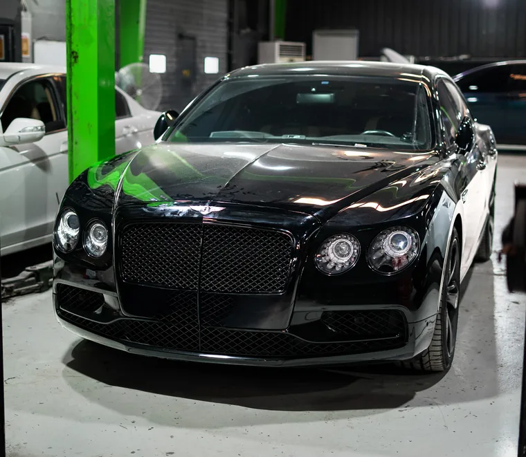 Black Bentley raised on a green two-post lift during a front-end inspection at Exotic Auto Services in Mussafah.