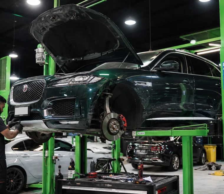 Jaguar SUV raised on a green two-post lift with the bonnet open in a workshop bay.