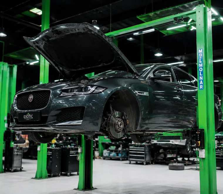 Jaguar SUV raised on a green two-post lift with a wheel removed for underbody and suspension work.