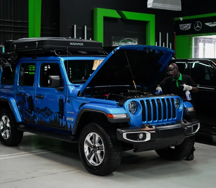 Blue Jeep Wrangler in the Exotic Auto Services workshop in Abu Dhabi while a technician works alongside it.