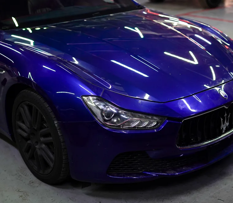 Blue Maserati Ghibli photographed close up at the front wing and headlight during inspection in the Mussafah workshop.