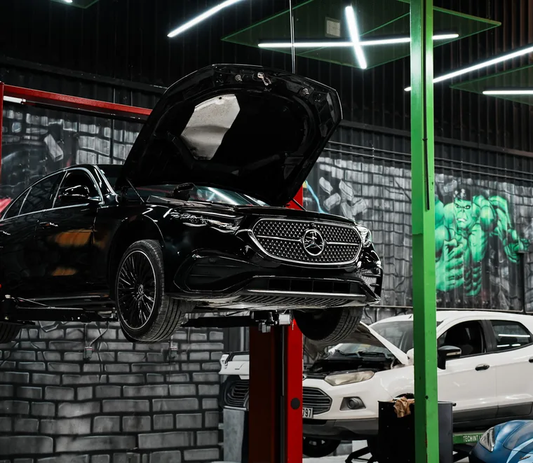 Black Mercedes-Benz raised on a lift with the bonnet open for engine bay access at the Exotic Auto Services workshop in Mussafah.