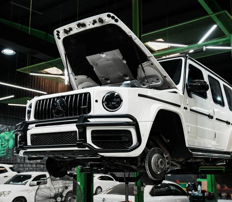 White Mercedes-AMG G-Class raised on a green two-post lift with the bonnet open at the Exotic Auto Services workshop in Mussafah, Abu Dhabi.