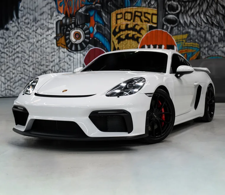 White Porsche 718 Cayman GT4 photographed from the front quarter inside the Exotic Auto Services workshop in Mussafah.