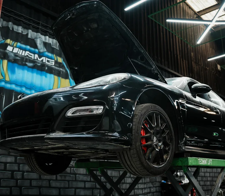 Dark Porsche raised on a two-post lift with the bonnet open at the Exotic Auto Services workshop in Mussafah, Abu Dhabi.