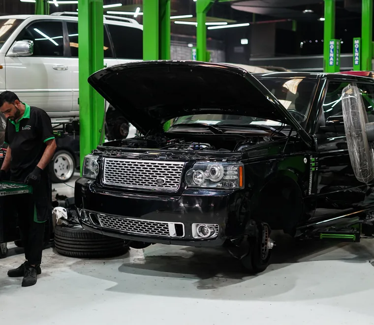 Exotic Auto Services technician working in the engine bay of a black Range Rover with the bonnet open in Mussafah, Abu Dhabi.