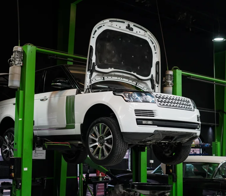 White Range Rover raised on a green two-post lift with the bonnet open at the Exotic Auto Services workshop in Mussafah.