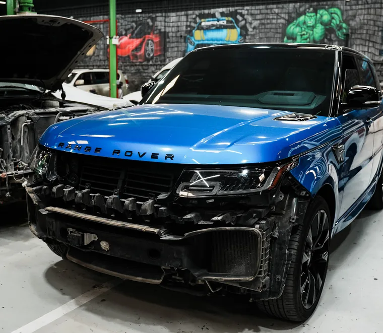 Blue Range Rover Sport with the front end stripped for body repair at the Exotic Auto Services workshop in Mussafah.