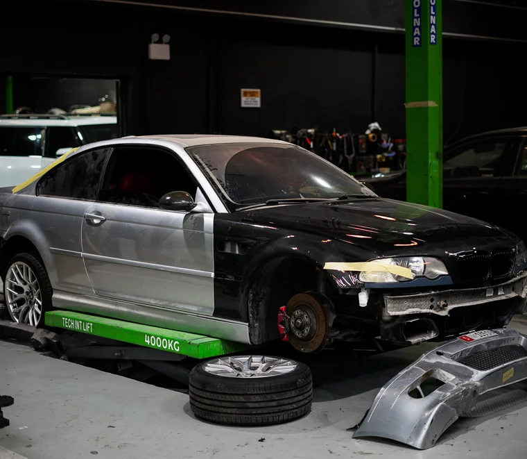 BMW coupe on a scissor lift with the wheels and front bumper removed for suspension and body work in Mussafah.