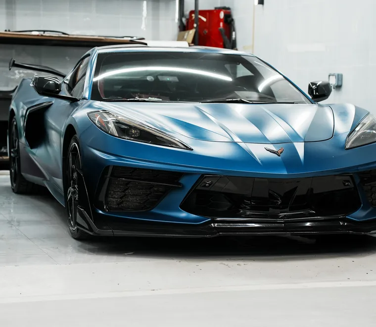 Blue Chevrolet Corvette C8 photographed from the front quarter inside the Exotic Auto Services workshop in Abu Dhabi.