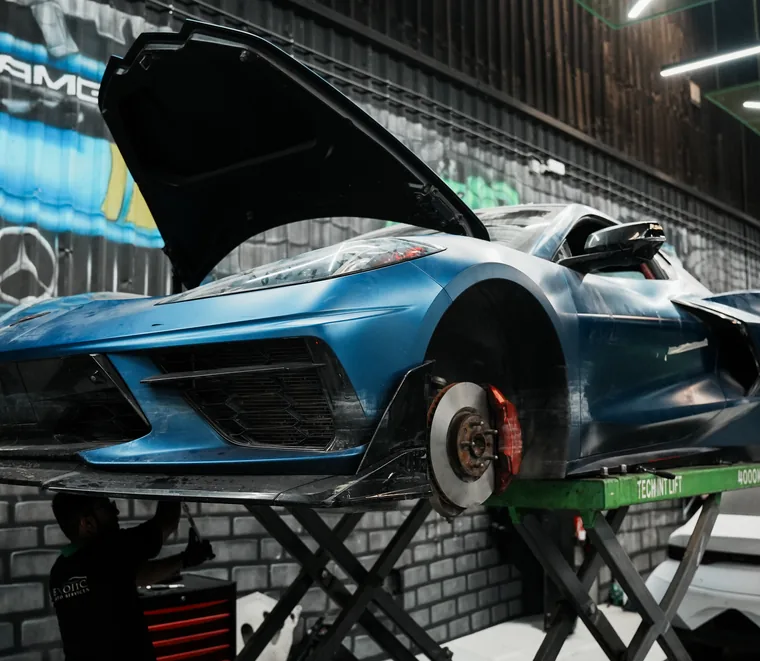 Blue Chevrolet Corvette raised on a lift with the rear clam open at the Mussafah workshop.