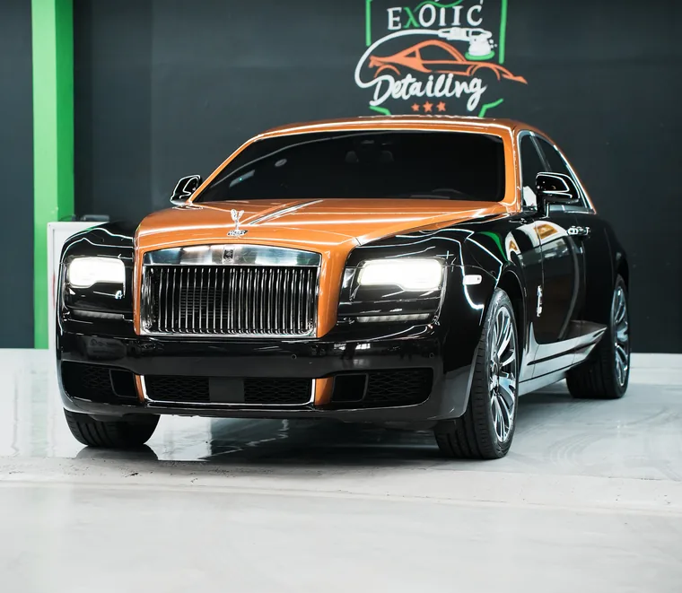 Two-tone orange and black Rolls-Royce seen from the front quarter in the detailing bay at the Mussafah workshop.